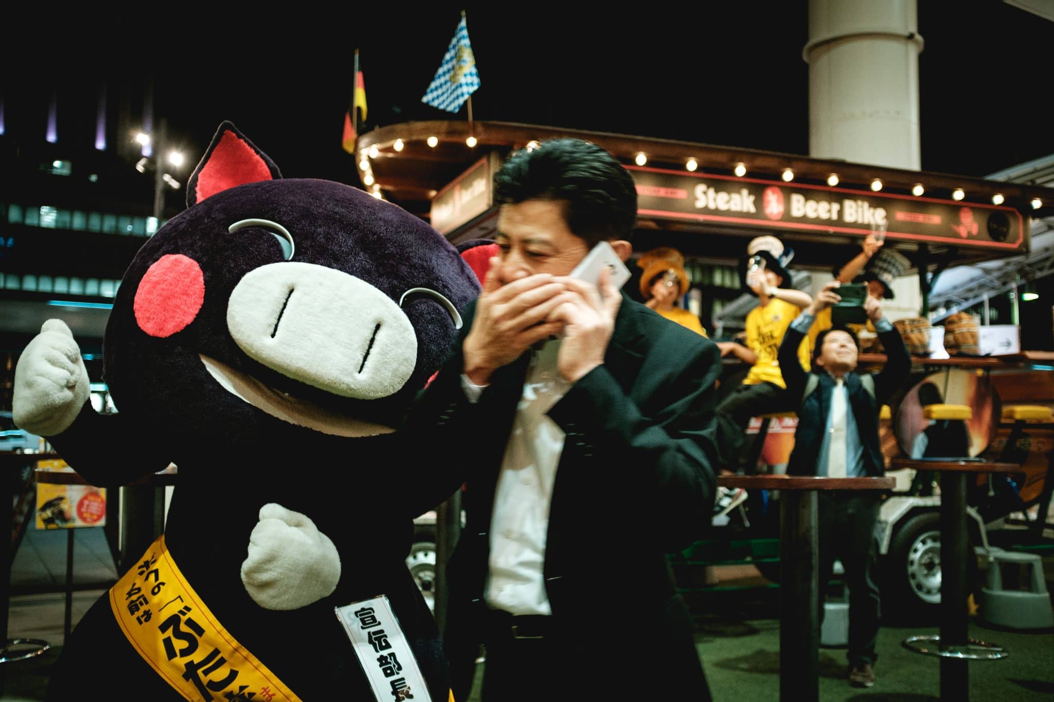 Japansk mand der taler i telefon ved siden af en yuru kyara maskot i grisekostume
