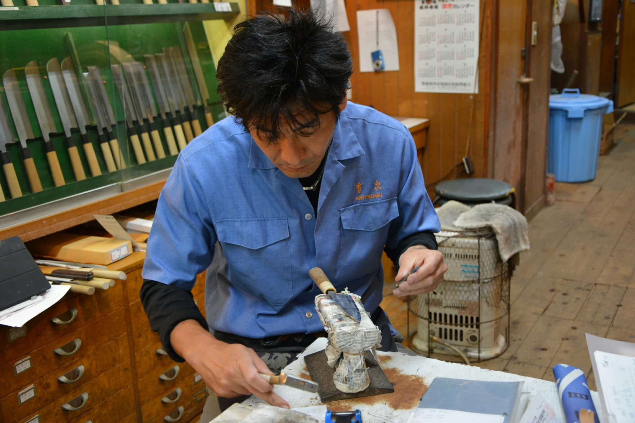 Japansk knivsmed sliber en japansk santoku kniv på en slibesten.